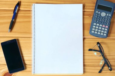 Üzerinde boş defter, cep telefonu, gözlük, kalem ve hesap makinesi olan rustik ahşap iş masasının yatay üst görüntüsü. Tasarımlar için merkez ofis modeli.