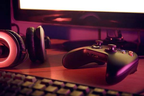 Siyah oyun sahası, kulaklık, klavye ve monitörlü oyun masası kurulumu görüntüsü kırmızı ve mor ışıklarla aydınlatılıyor.