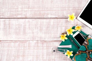 Moda kadın aksesuarları. Lüks el yapımı yılan derisi (python) el çantası, tablet, smartphone, plumeria. Üstten Görünüm, düz yatıyordu, açık ahşap renkli. Metin için ücretsiz/boş yer.