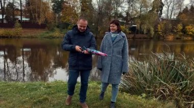 Sonbahar zamanı göletli parkta şemsiyeyle yürüyen genç bir çift. Güzel yavaş çekim görüntüleri.