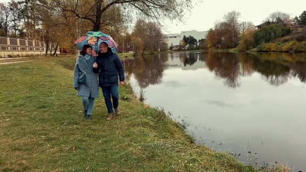 Jeune couple avec parasol promenade dans le parc avec étang à l'automne. Belle séquence au ralenti. — Video