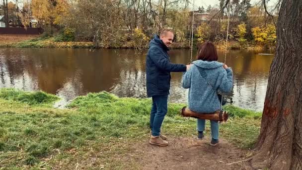 Jonge vrouw zwaait, haar man helpt haar. Mooie romantische slow motion beelden. Herfstpark. — Stockvideo