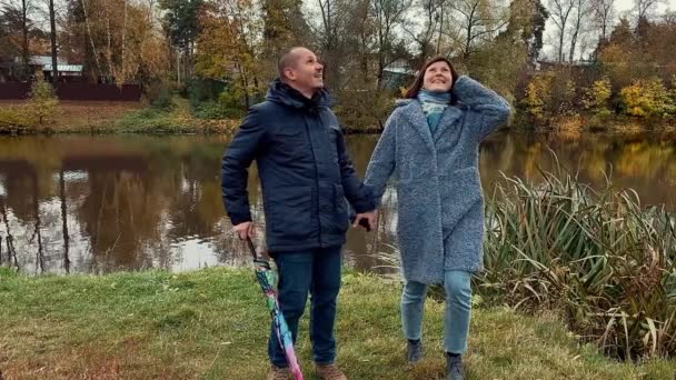 Jovem casal com guarda-chuva caminhar no parque com lagoa no outono. Lindas filmagens em câmera lenta. — Vídeo de Stock