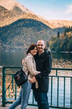 Genç çift dağlarda göl kenarında öpüşüyor ve sarılıyorlar..