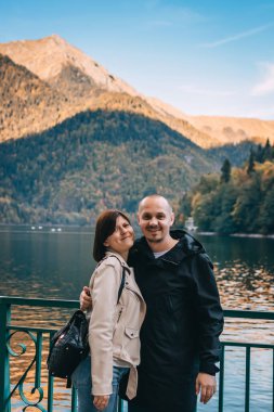 Genç çift dağlarda göl kenarında öpüşüyor ve sarılıyorlar..