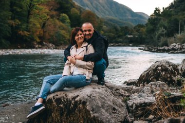 Genç çift dağlarda göl kenarında öpüşüyor ve sarılıyorlar..