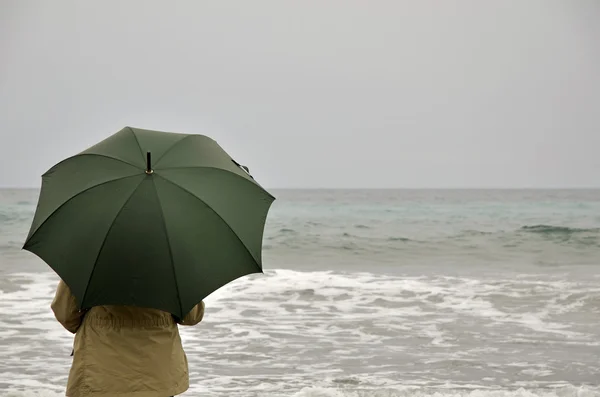 Woman with green umbrella on the beach on a rainy day — Stock Photo, Image