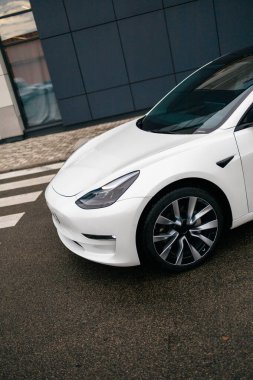 KYIV, UKRAINE - 20 Temmuz 2025: Beyaz bir Tesla Model 3 arabası bir binanın ön cephesinde büyük bir Decathlon reklam afişinin önünde park edilmiş.