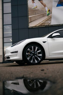 KYIV, UKRAINE - 20 Temmuz 2025: Beyaz bir Tesla Model 3 arabası bir binanın ön cephesinde büyük bir Decathlon reklam afişinin önünde park edilmiş.