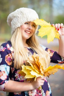 Akçaağaç yapraklı, sıcak şapkalı güzel bir kız gülümsüyor..