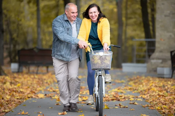 Happy middle aged couple with bike in autumn park. Elderly cheerful husband and wife on a walk.