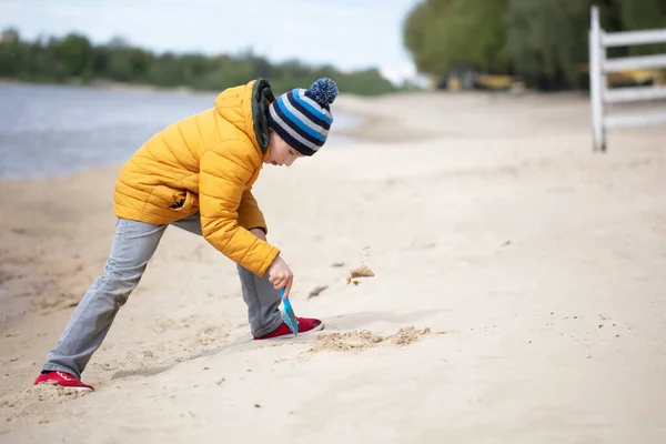 Το αγόρι με τα φθινοπωρινά ρούχα παίζει στην παραλία. — Φωτογραφία Αρχείου