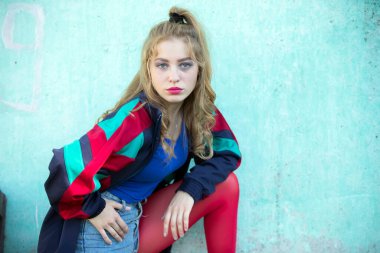 Kız doksanlı yılların tarzında giyinmiş. Güzel, parlak bir kadın, kırmızı taytlı ve spor pantolonlu..