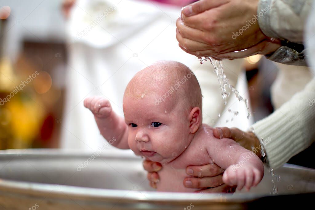 Orthodox baptism of a child.Baby in the baptismal font in the church. The hands of the priest pour water on the child during the ceremony of accepting faith.