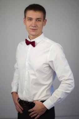 Gri arka planda genç bir adamın klasik portresi. 20 yaşlarında beyaz gömlekli ve papyonlu bir adam..