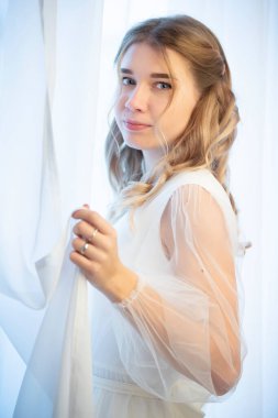 Beyaz perdelerin yanında güzel bir gelin. Beyaz arka planda güzel bir kızın dikey portresi..