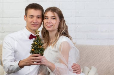 Gelin ve damat kanepede oturuyorlar ve bir Noel ağacı tutuyorlar. Noel Düğünü.