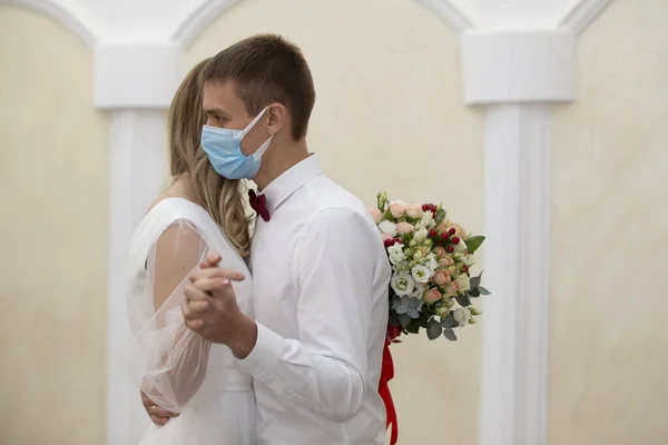 The bride in a medical mask with a bouquet of flowers is dancing with the groom. Wedding during the coronavirus panademia.