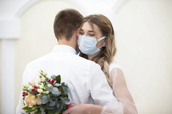 The bride in a medical mask with a bouquet of flowers is dancing with the groom. Wedding during the coronavirus panademia.