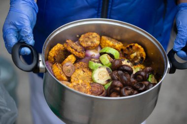 Şefin elleri ızgara sebze ve mantarlı bir tencere tutuyor..