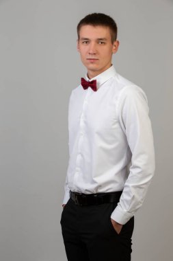 Gri arka planda genç bir adamın klasik portresi. 20 yaşlarında beyaz gömlekli ve papyonlu bir adam..