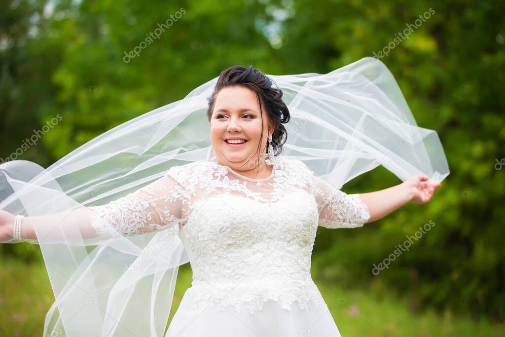 Portrait of a plump bride with a waving veil against a background of summer greenery.