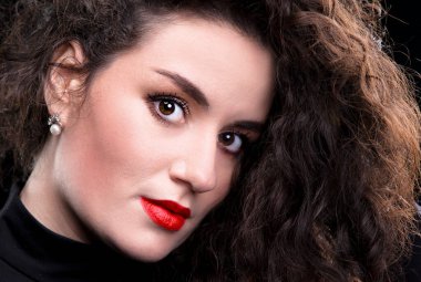 Kıvırcık saçlı ve parlak makyajlı esmer bir kızın yakın plan fotoğrafı..