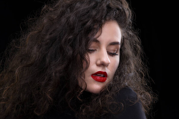 Beautiful brunette girl with curly hair and bright makeup on a dark background.
