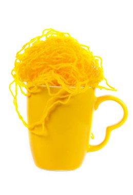 Beyaz arka planda sarı iplikçikler olan sarı bir bardak..