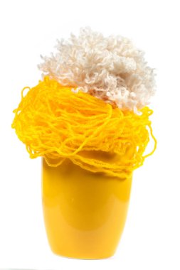 Beyaz arka planda örgü örmek için iplik yumakları olan sarı bardak. İğne işi.