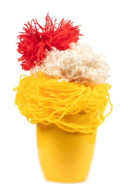 Beyaz arka planda örgü örmek için iplik yumakları olan sarı bardak. İğne işi.