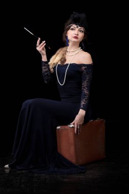 Geçen yüzyılın 20-30 'ları tarzında giyinmiş güzel bir kız. Elinde puro ve koyu bir arka planda bavul var. Klasik retro kız..