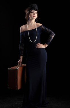 Geçen yüzyılın 20-30 'ları tarzında giyinmiş güzel bir kız. Elinde puro ve koyu bir arka planda bavul var. Klasik retro kız..