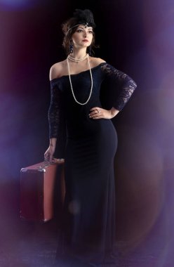 Geçen yüzyılın 20-30 'ları tarzında giyinmiş güzel bir kız. Elinde puro ve koyu bir arka planda bavul var. Klasik retro kız..