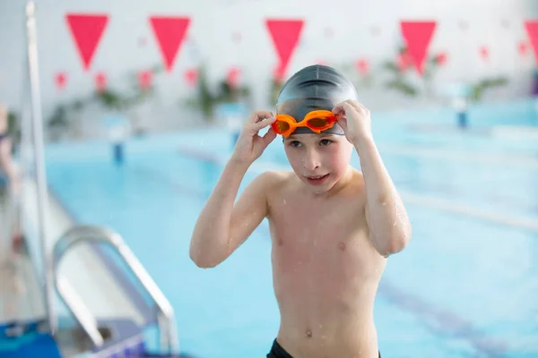 Boy in a swimming cap and swimming goggles in the pool. The child is engaged in the swimming section.