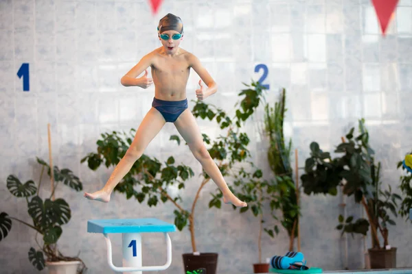 A child in a cap and swimming goggles jumps into the pool. Swimming section.