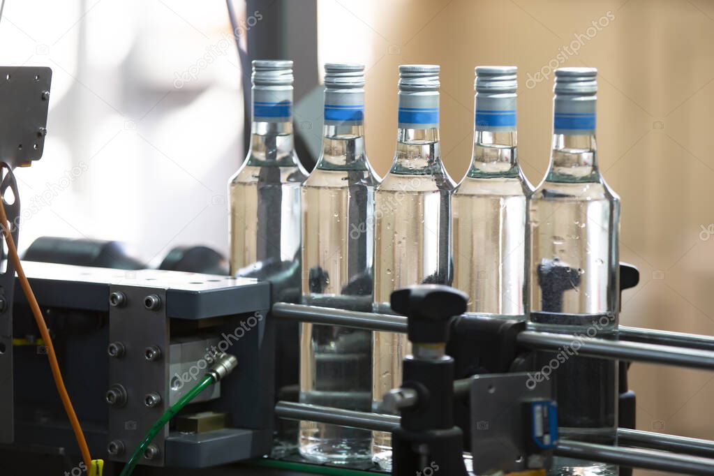 A long row of glass bottles on a conveyor belt. Production of alcoholic beverages.
