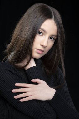 Koyu bir arka planda uzun saçlı, 17 yaşında güzel bir kızın dikey portresi..
