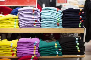 There are stacks of knitted sweaters, folded longsleeves or T-shirts on a store shelf. Selling clothes in a store. clipart