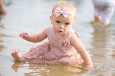 Güzel küçük bir kız nehir kıyısında oturur ve kum ve suyla oynar. Çocuk ve doğa.