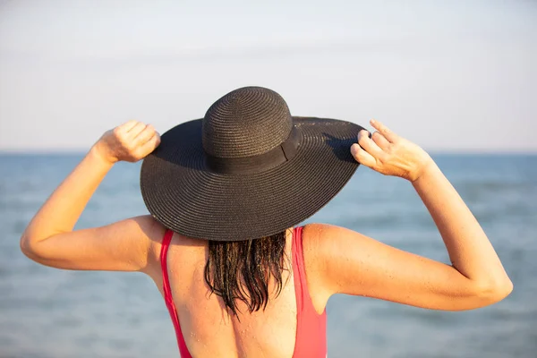Eine Frau Mit Breitkrempigem Hut Und Badeanzug Blickt Aufs Meer — Stockfoto