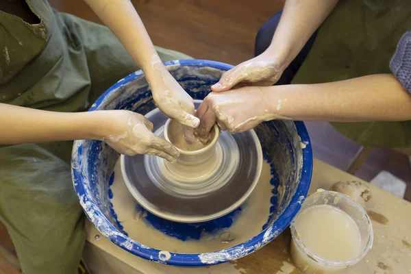 Close-up of a potter\'s hands and a child\'s hand with an item on a potter\'s wheel. Working with clay. Clay workshop. Craft training.