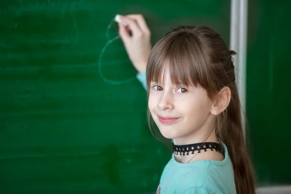 教室で子供の学生 緑のボードの幸せな女子学生が何かを書いている — ストック写真