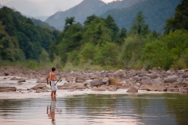 Elinde olta olan bir çocuğun balık tuttuğu dağ gölü manzarası. Sırtı kameraya dönük duruyor..