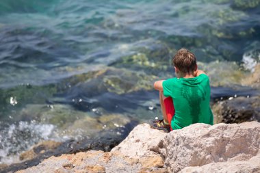 Amalchik sırtı kameraya dönük bir şekilde oturur ve denize bakar..