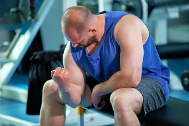 Spor salonunun arka planında kaslarına bakan atletik bir adam..