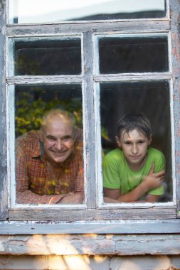 Büyükbaba ve torun bir köy evinin penceresinden bakıp gülümsüyorlar. Babalar Günü. Oğlan ve adam pencerede.
