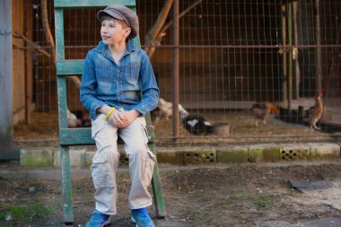 Bir tavuk kümesinin arka planında şapka ve kot ceketli klasik köylü çocuk.