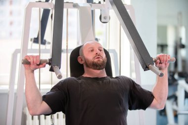 Bir adam spor salonunda çalışıyor, ağırlık kaldırıyor ve makine kullanıyor. Odaklanmış ve kararlı, muhtemelen gücünü ve uygunluğunu geliştirmeye çalışıyor.