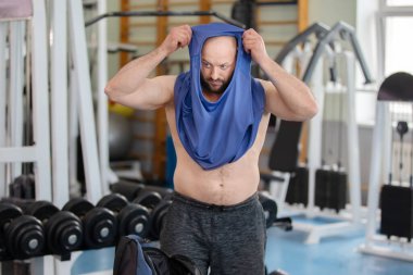 Spor salonunda bir adam idmandan sonra mavi tişört giyer..